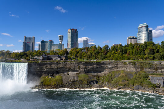 View of Niagara Falls' powerful cascade against the backdrop of the city's skyline, a contrast of nature's raw force and urban development, Niagara Falls, Ontario, Canada.
