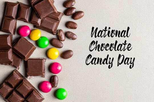 An overhead view shows an assortment of chocolate bars, colorful candies, and chocolate-covered almonds on a light canvas backdrop with a playful handwritten note for national chocolate candy day