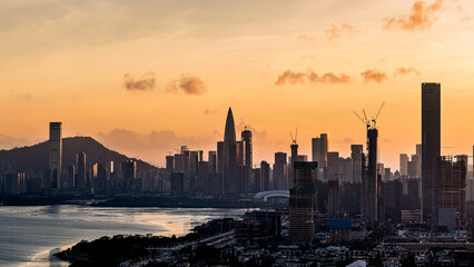 Naklejka premium City skyline with modern skyscrapers silhouetted against a vibrant sunset sky in Shenzhen.