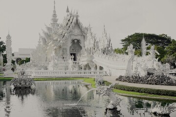 Majestic White Temple (Wat Rong Khun) in Chiang Rai, Thailand, featuring intricate architecture and a stunning mirror reflection on a calm pond under a clear blue sky.