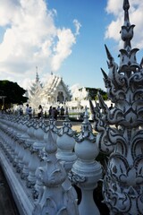 Detailed exterior view of the ornate white plasterwork and glass mosaics of Wat Rong Khun temple, showcasing traditional Thai motifs with a modern artistic twist.