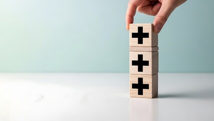 A hand stacking wooden blocks with black plus signs on a clean white surface with a light blue background precisely