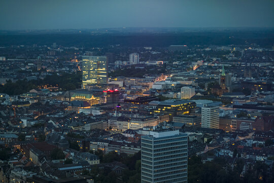 Aerial view of city lights twinkle across the cityscape, highlighting the modern architecture and historic church spires at dusk, Dusseldorf, North Rhine-Westphalia, Germany.
