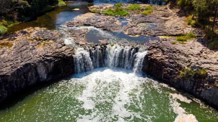 Aerial view of the cascading Haruru Falls plunges into a vibrant green pool, framed by rugged rocks and lush foliage, Haruru Falls, Bay of Islands, New Zealand.