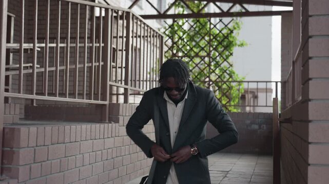 urban hallway with brick walls and iron rails frames and stylish man in coat and white sneakers, tightening buttons while stepping down stairs, showing trellis greenery behind and clean symmetry