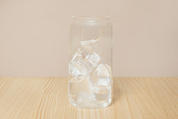 A clear glass filled with ice on a light wooden table