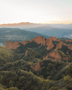 View of ochre-colored ancient Roman gold mine contrasting with green trees under a pastel sky, Las M&eacute;dulas, Castilla y Le&oacute;n, Spain.