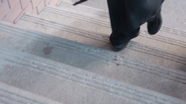 lower frame shows female in dark coat stepping up stair beside brick post and iron guard, brown handbag swinging, focus on corridor view, movement captured from above with emphasis on legs and motion
