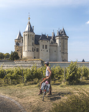View of a man pauses with his bicycle near a vineyard, the Chateau de Saumur rising majestically in the background, Saumur, Pays de la Loire, France.