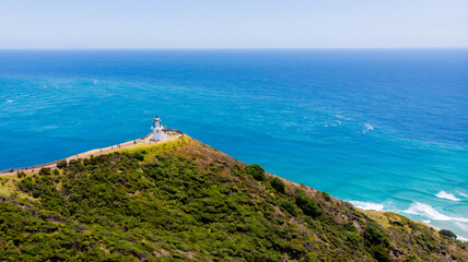 Aerial view of the iconic Cape Reinga Lighthouse perched dramatically on a headland where the Tasman Sea meets the Pacific Ocean, Cape Reinga, Northland Region, New Zealand.