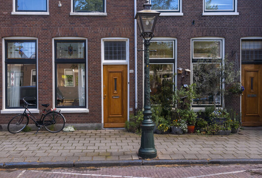 View of brick buildings stand proudly with a bicycle parked beside a window, flowers adding pops of color, and a street lamp illuminating the scene, Leiden, South Holland, Netherlands.