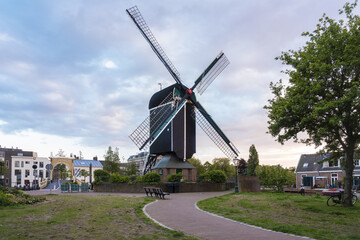 View of a classic Dutch windmill rises majestically over a winding path in a park setting under a serene sky, Leiden, South Holland, Netherlands.