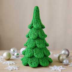 Knitted green Christmas tree with holiday ornaments and snowflakes on a wooden surface for winter festive decoration and seasonal celebration.