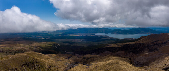 Aerial view of rugged terrain meets the tranquil blue waters of Lake Rotoaira under a sky heavy with dramatic clouds, Tongariro National Park, Manawatu-Whanganui Region, New Zealand.