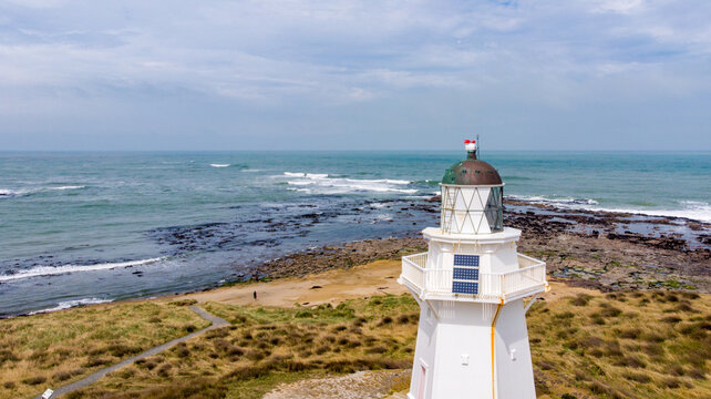 Aerial view of the striking white Waipapa Point Lighthouse standing tall against the rugged coastline and vast ocean, Waipapa Point Lighthouse, Southland Region, New Zealand.
