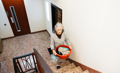 Senior woman carrying laundry basket climbing apartment stairs