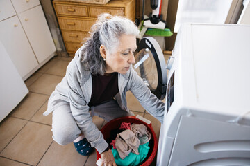 Senior woman doing laundry with washing machine at home