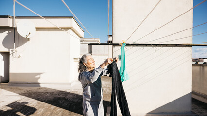 Senior woman hanging laundry on rooftop clothesline