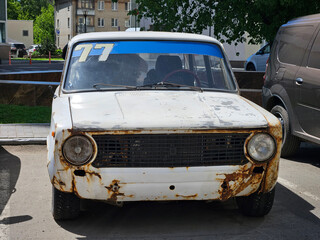 White car with the number 77 on the windshield. The car is parked in a parking lot