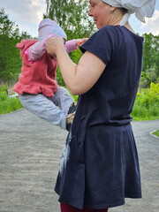 Woman is holding a baby in her arms. The baby is wearing a pink hat. The woman is wearing a black dress
