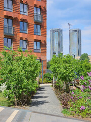 Brick building with a green path in front of it. The path is lined with trees and bushes near twin construction