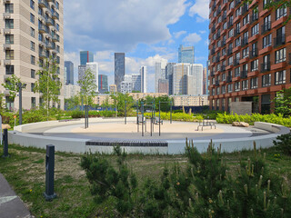 Park with a large circular area in the middle. There are benches and a few trees. The park is surrounded by buildings near entrance in the courtyard of the house in residential complex