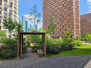 Bench is in a park next to a building. The bench is wooden and is located in front of a building near entrance in the courtyard of the house in residential complex