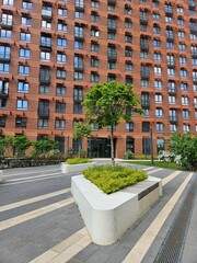 Brick building with a tree in front of it. The tree is in a planter. The building has many windows near entrance in the courtyard of the house in residential complex