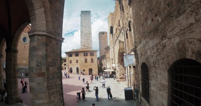 Piazza della Duomo square of San Gimignano in Tuscany, Italy with medieval architecture stone tower, and numerous tourist people visitors sightseeing, aerial view