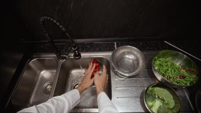 POV shot of male chef washing vegetables arranged in stainless steel bowls rinsing tomatoes, broccoli and rocket while cooking fresh salad in commercial kitchen