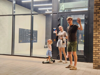 Man and a woman are standing in front of a building with a child on a skateboard