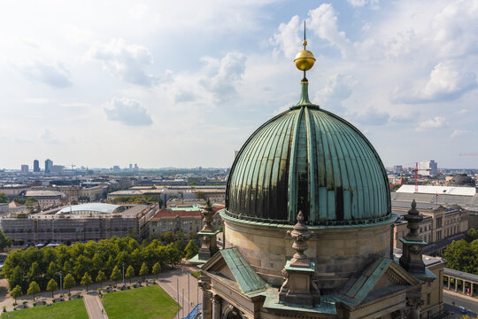 View of the contrasting weathered copper dome and the golden spire, standing tall against the urban skyline in Mitte, Berlin, Germany.