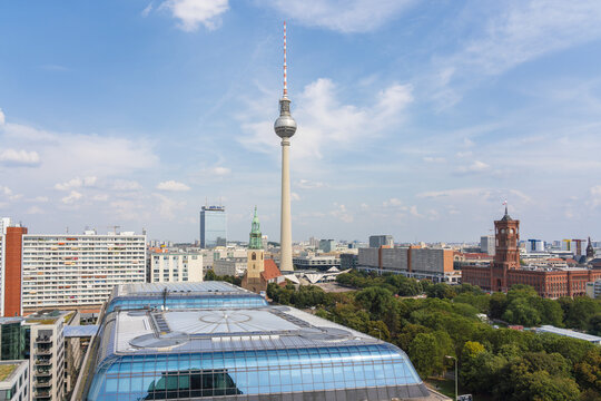 View of a towering TV tower piercing the bright blue sky, amidst a diverse cityscape of modern buildings and historic architecture, Mitte, Berlin, Germany.
