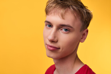 Man, face, youth, calm, smile, red shirt, yellow background, studio, closeup, headshot with soft light highlighting clear skin and blonde hair for a modern friendly stock image