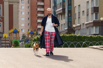 Man walks dog, Man in pajamas leisurely walks his dog through city gardens, Relaxed individual dressed comfortably walks his small beagle past residential blocks in city during peaceful morning