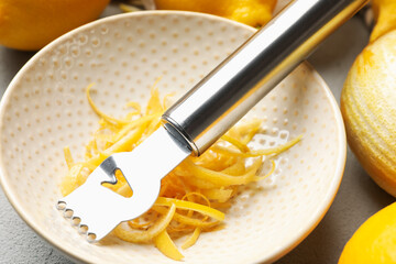 Fresh lemons with zest and zester tool on grey table, closeup