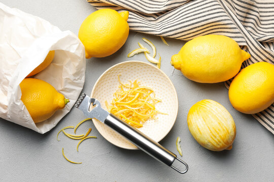 Fresh lemons with zest and zester tool on grey table, flat lay