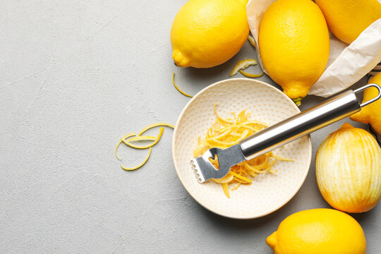 Fresh lemons with zest and zester tool on grey table, flat lay. Space for text