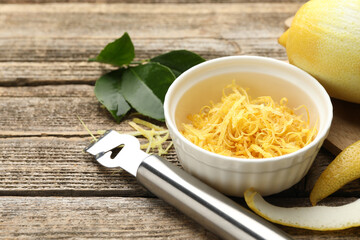 Bowl with lemon zest, fresh fruit, leaves and zester on wooden table, closeup. Space for text