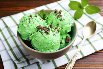 Tasty mint chocolate chip ice cream, spoon and towel on wooden table, closeup