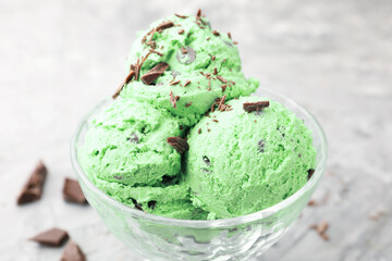 Tasty mint chocolate chip ice cream on grey textured table, closeup