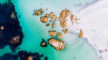 Aerial view of the vibrant turquoise water swirling around the rust-colored rocks contrasting with the white sandy beach., Bay of Fires, Tasmania, Australia.
