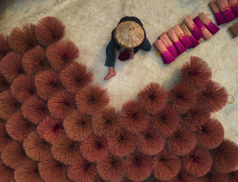 Aerial view of a person arranging bundles of incense sticks in a circular design on the ground, creating a vibrant display of color and texture, Hanoi, Hanoi, Vietnam.