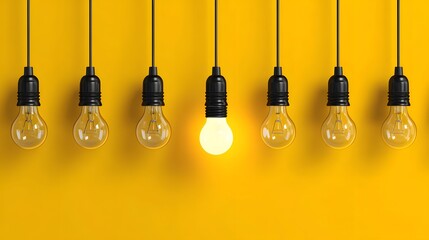 Row of hanging incandescent bulbs against a bright yellow background features one illuminated light source