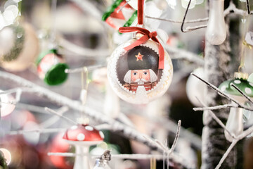 Holiday decorations in the form of balls with a Nutcracker design on the branches of a Christmas tree in light colors