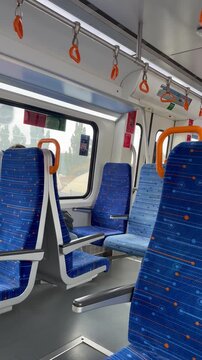 Interior de un tren en movimiento con asientos azules y naranja.