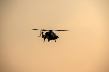 Silhouette helicopter is coming on isolated sky during dawn