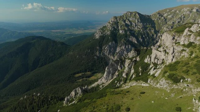 Aerial flight along the western slopes of Bucegi Mountains, revealing the steep Gutanu and Lancia peaks, opening to the dramatic Gaura Valley with steep limestone cliffs and erosion towers, Romania