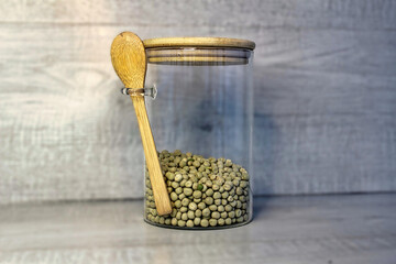 A jar of beans is sitting on a wooden table with a spoon inside