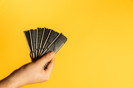 Hand holding fan of black DDR RAM sticks on yellow background, upgrade concept. High quality photo